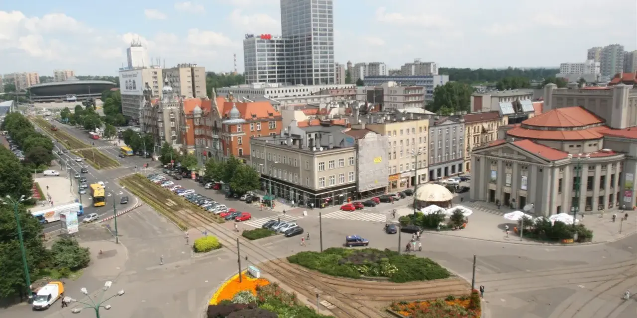 Widok na ruchliwy rynek w Katowicach z tramwajami, samochodami i budynkami.
