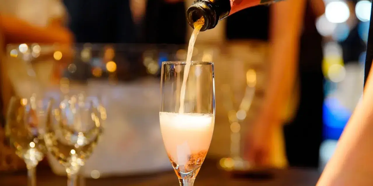 Nalewanie musującego **cava wino** do kieliszka. W tle widać inne kieliszki i rozmyte światła, sugerujące uroczystą atmosferę.