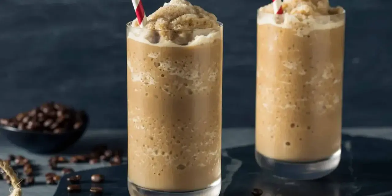 Dos vasos altos con granizado de café, decorados con pajitas rojas y blancas. Un tazón de granos de café en el fondo.