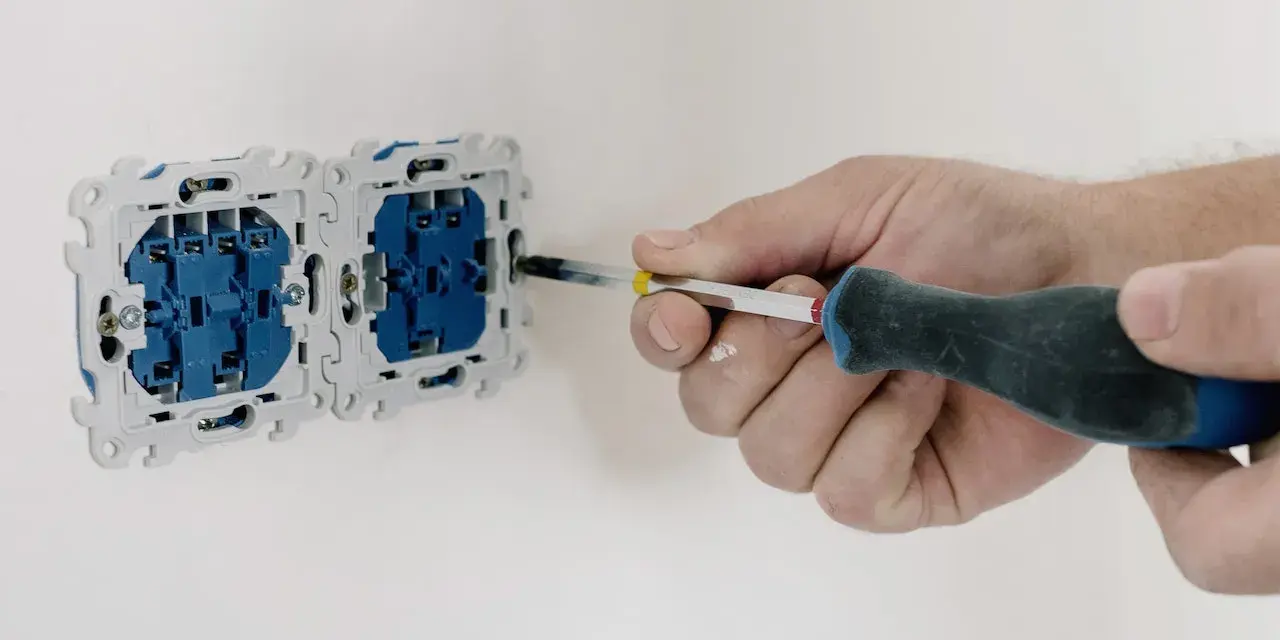 Dłoń przykręca gniazdko śrubokrętem. Kluczowe jest sprawdzenie rezystancji izolacji przed podłączeniem zasilania.