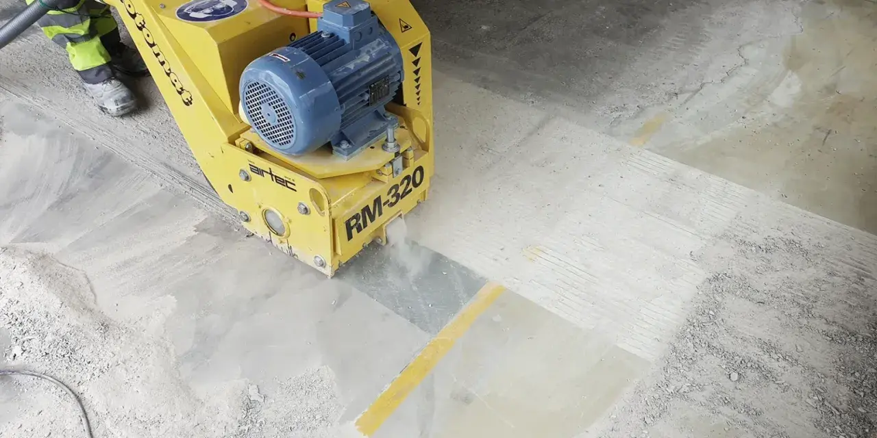 Żółta maszyna do szlifowania betonu RM-320 pracuje na posadzce, tworząc pył.