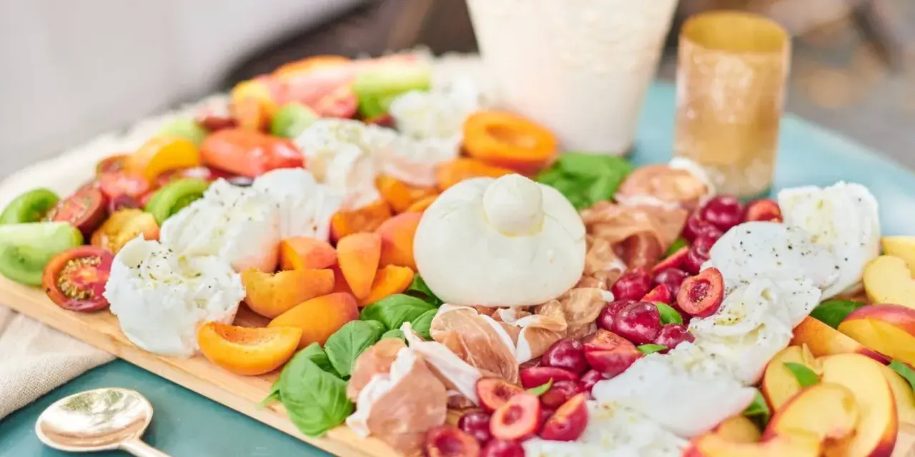 Eine bunte Antipasti Platte anrichten mit Burrata, Kirschen, Pfirsichen, Tomaten und Prosciutto.