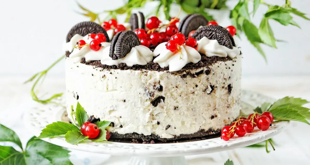 Pyszny tort z kawałkami oreo ciastka, udekorowany bitą śmietaną i czerwonymi porzeczkami.