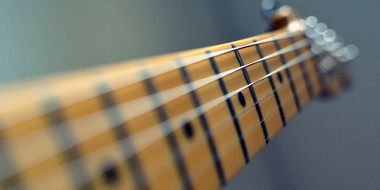 Zbliżenie na gryf gitary, gdzie ja gram na gitarze chwyty. Widać struny i progi.