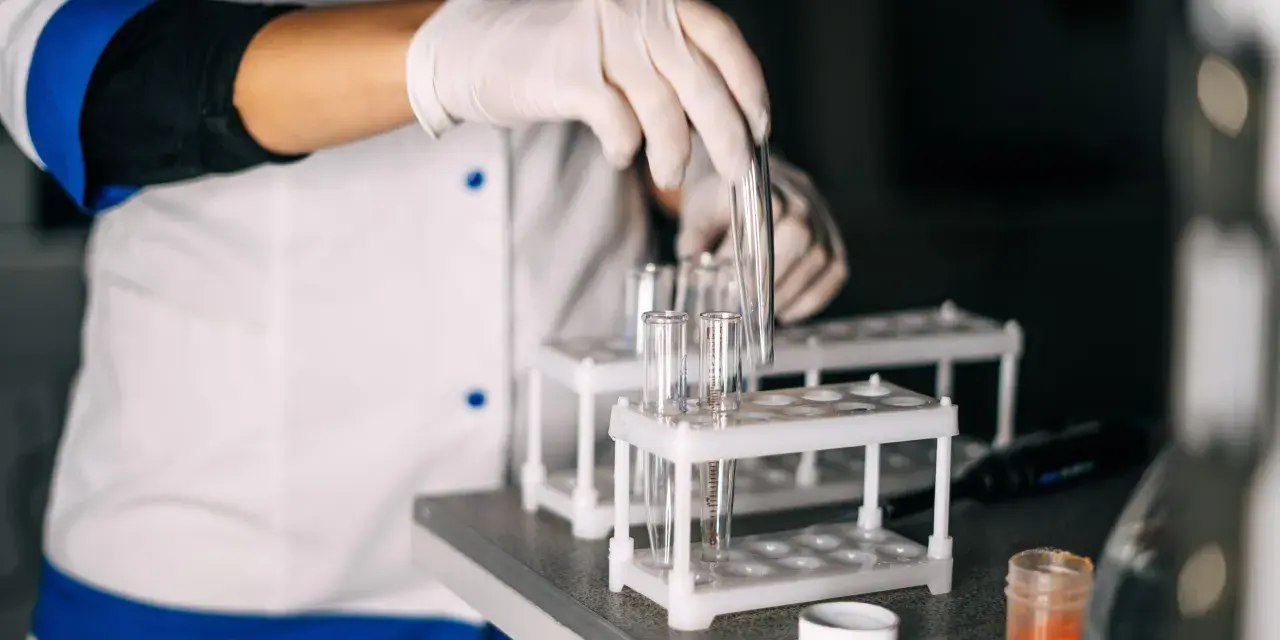 Laborant med handskar hanterar provrör. Kanske för att ta testosteron eller analysera andra prover i labbet.