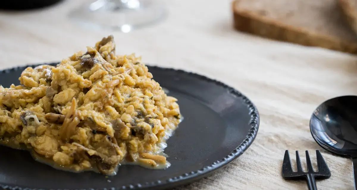 Delicioso revuelto de setas servido en plato oscuro, acompañado de pan y cubiertos.