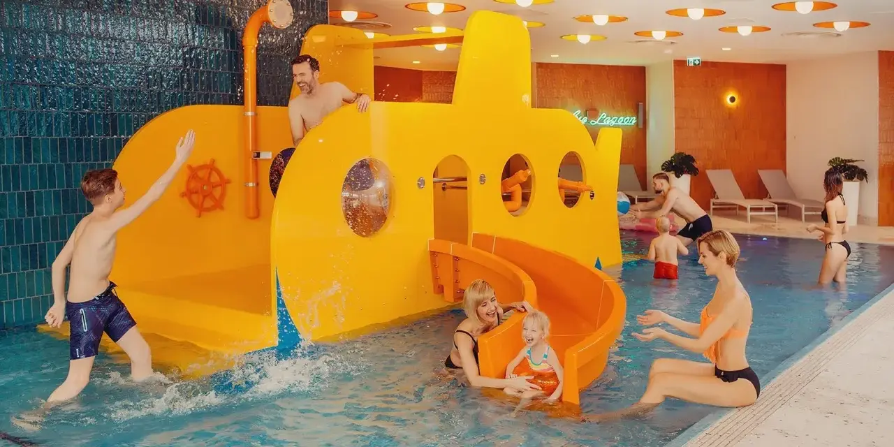 Rodzina bawi się w hotelu z aquaparkiem dla dzieci w górach. Żółta łódź podwodna ze zjeżdżalnią to centrum wodnych atrakcji.
