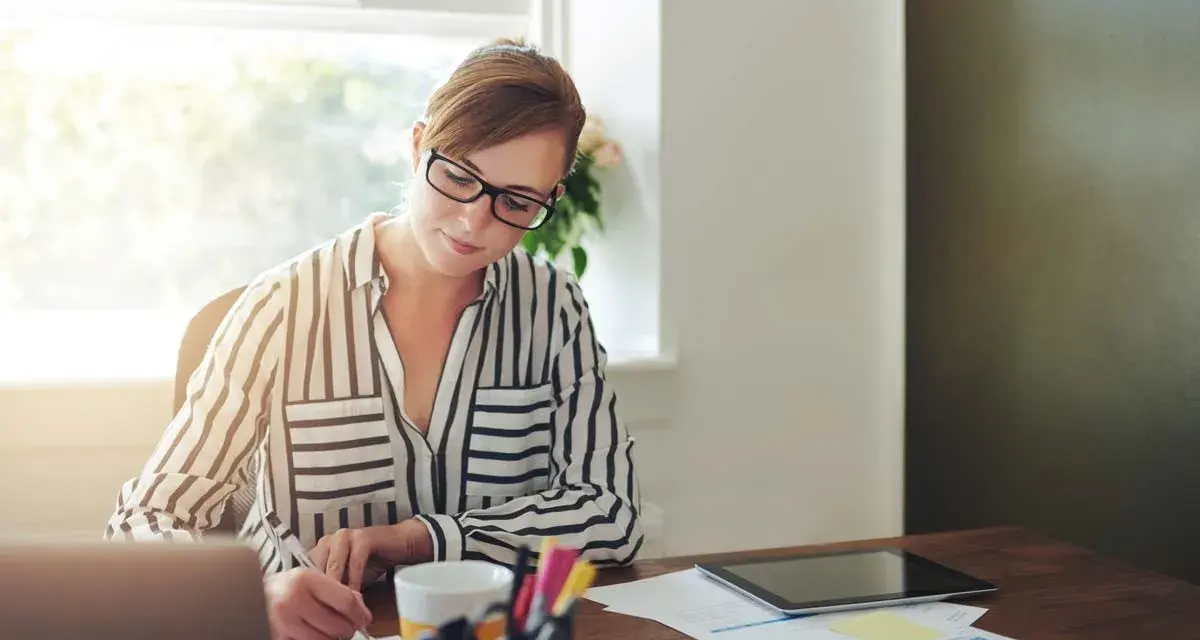 Mujer con gafas trabaja en su escritorio, revisando documentos y gráficos. Quizás está lidiando con gastos de difícil justificación.