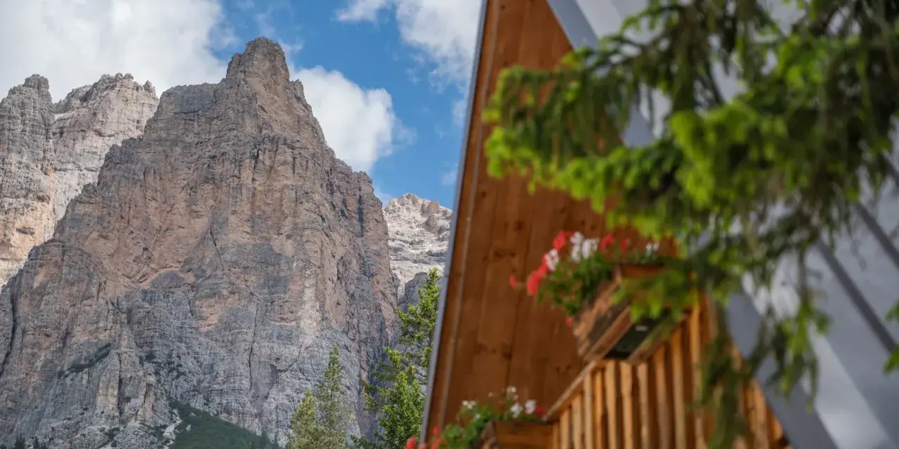 Drewniany domek z kwiatami w skrzynkach na tle skalistych Dolomitów.