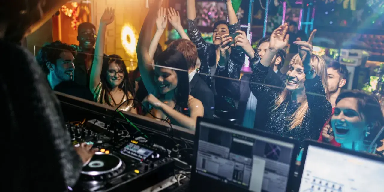 Feiernde Menschen tanzen im Club, während ein DJ auflegt. Eine druckbare muttizettel vorlage zum ausdrucken wäre hier perfekt für die nächste Party!