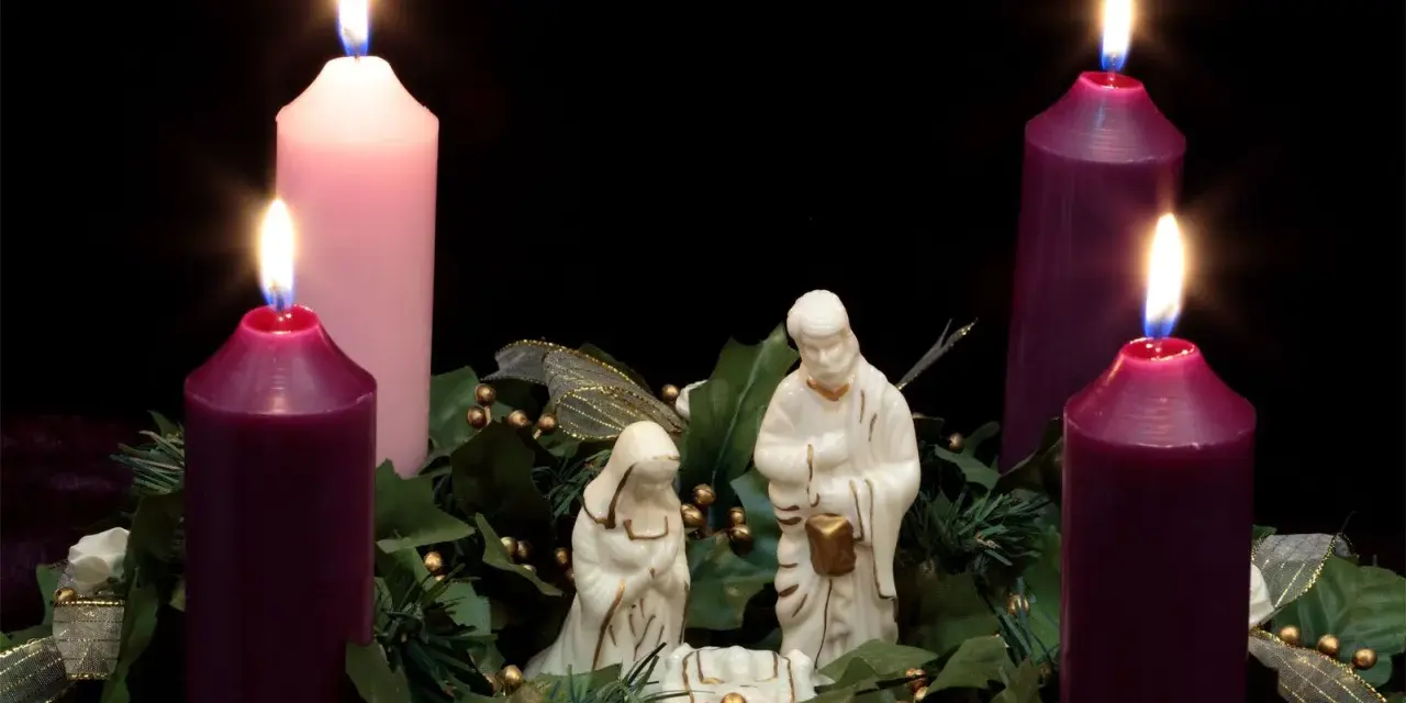 Three lit candles, two purple and one pink, surround a nativity scene. This is the advent 3rd Sunday.