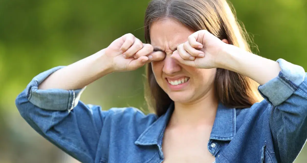 Ragazza con espressione infastidita, si stropiccia gli occhi con le mani, forse per il sole o per la stanchezza.