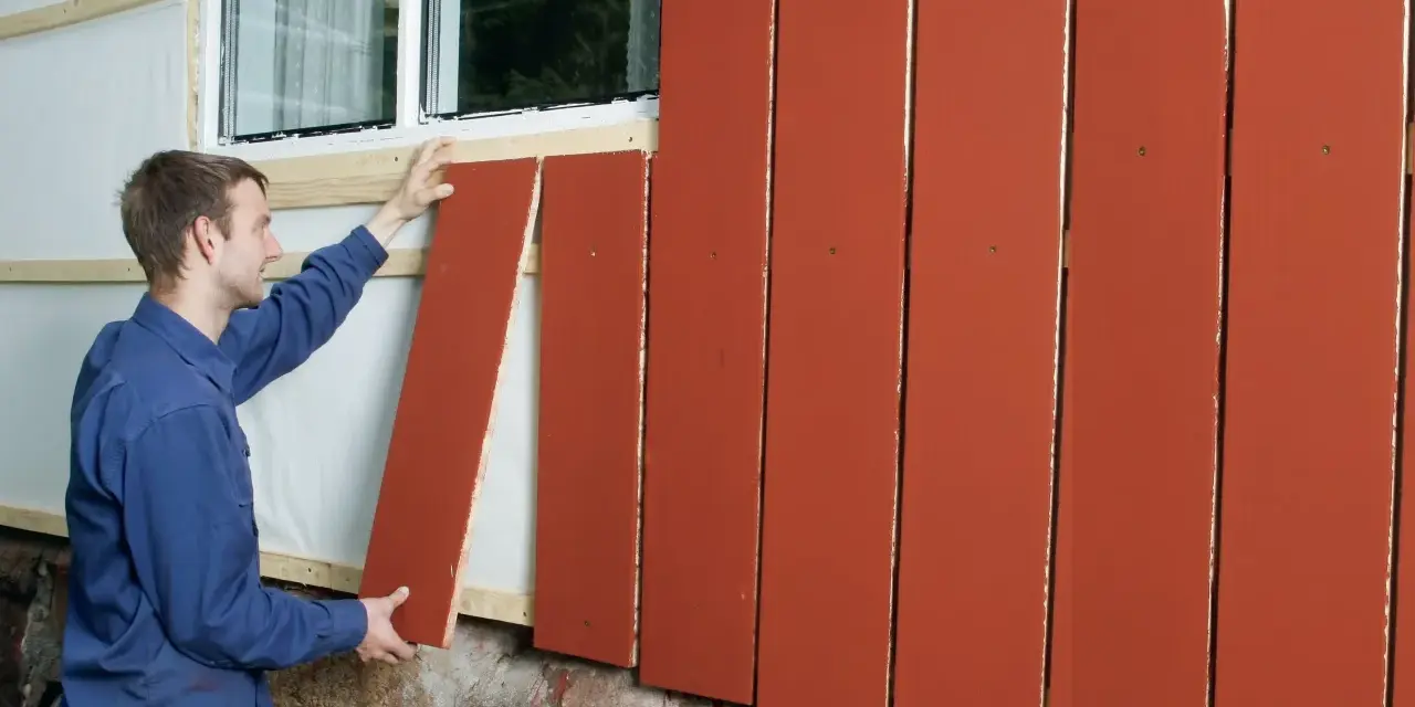 Man monterar en röd lockpanel vid ett fönster.
