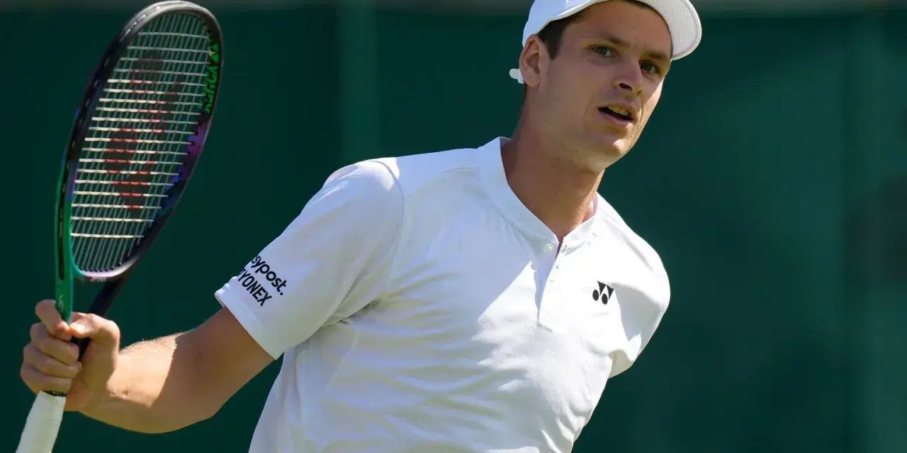 Hubert Hurkacz w białej koszulce i czapce, gotowy do uderzenia rakietą na Wimbledonie.