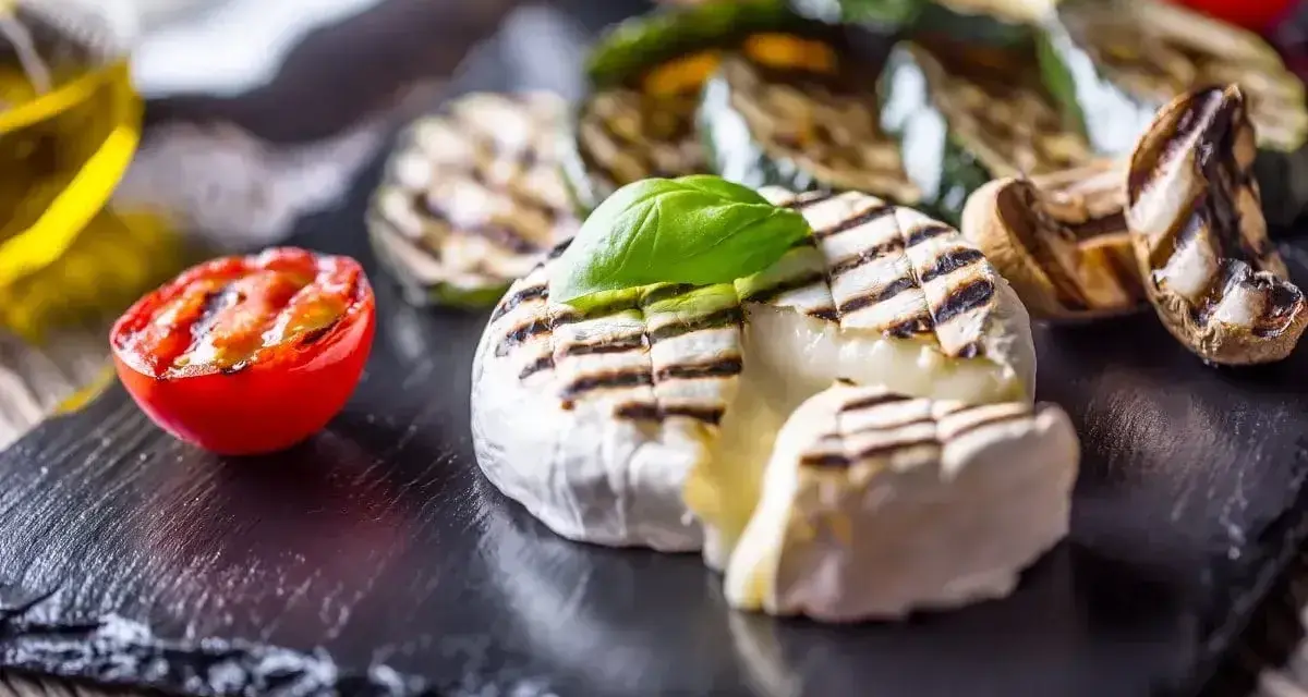 Pyszny camembert z grilla, z rumianymi paskami, podany z grillowanymi warzywami i pomidorkiem.
