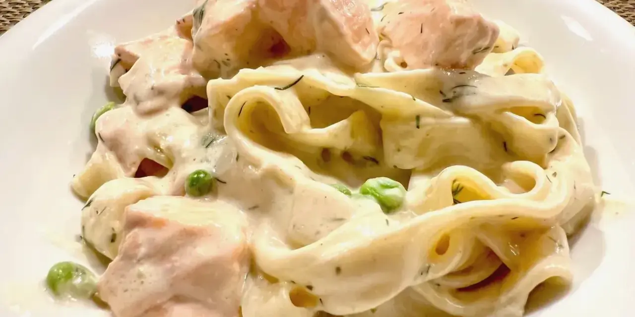 Cremige Nudeln mit Lachs, Erbsen und Dill in einer weißen Schüssel.