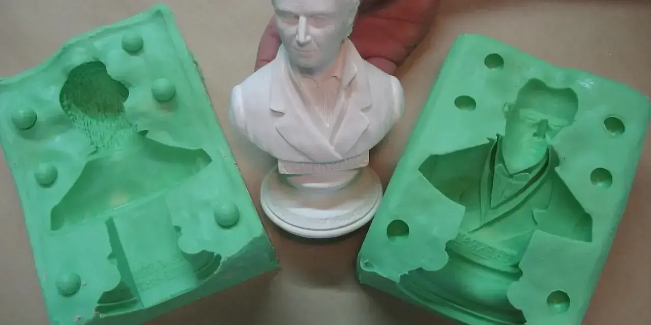 Making silicone molds for resin casting. A white bust is held between two green silicone molds, ready to capture its detail.