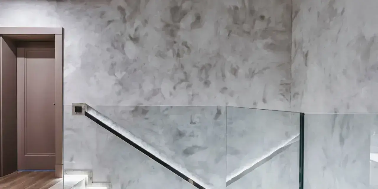 Nowoczesny hol z podświetlanymi schodami i szklaną balustradą. Efektowny tynk na ścianie dodaje wnętrzu elegancji.
