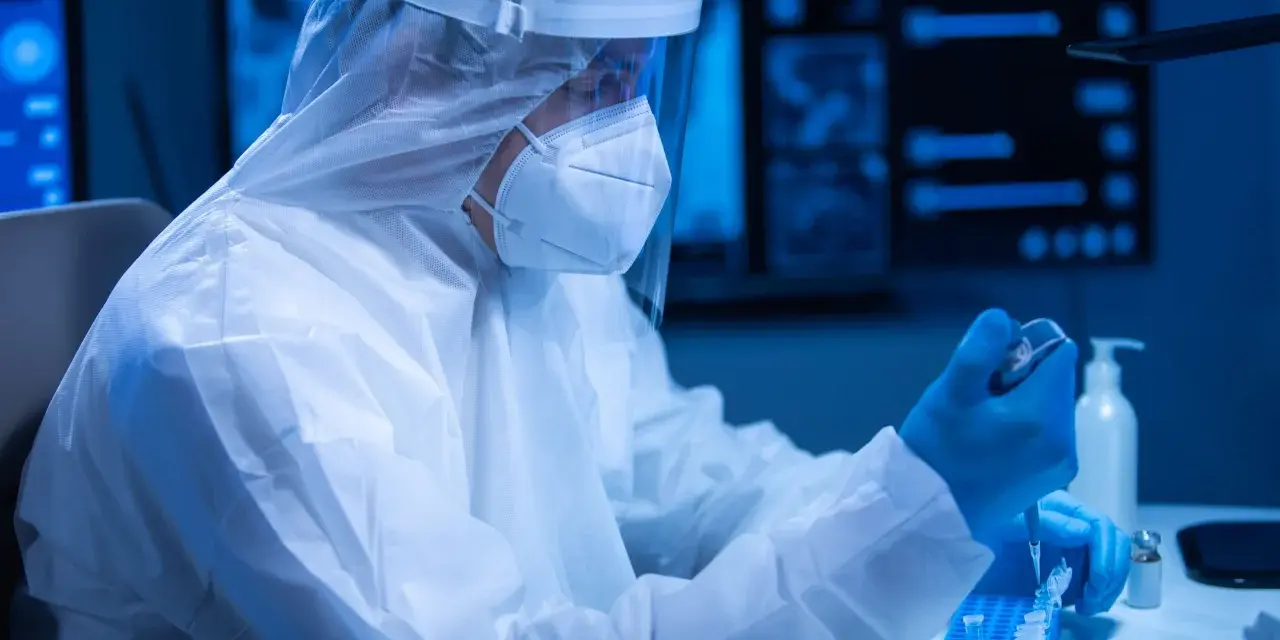 Badacz w kombinezonie ochronnym pracuje w laboratorium, przygotowując próbki. Czas oczekiwania na wynik badania PCR może być różny.