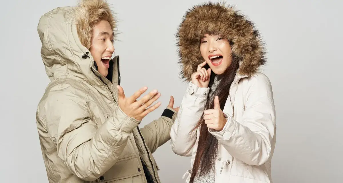 Pareja feliz con abrigos de invierno, ¡el mejor abrigo para el frío! Ella da pulgar arriba, él gesticula.