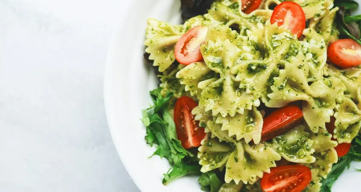 Pyszny makaron farfalle z aromatycznym pesto i soczystymi pomidorkami koktajlowymi, podany na liściach sałaty.