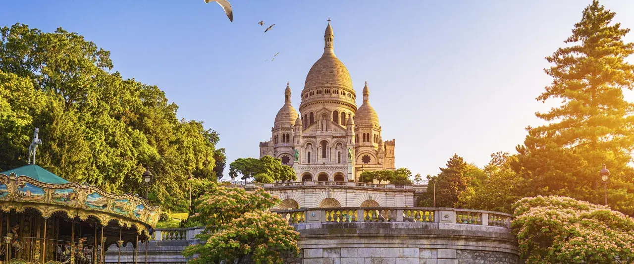 El barrio Montmartre, con la basílica del Sacré-Cœur al fondo, un carrusel y árboles frondosos bajo un cielo azul.