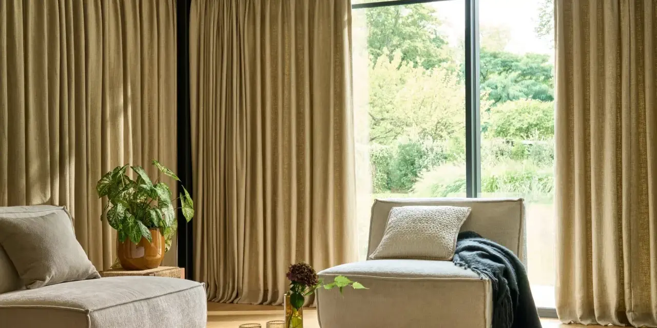 Salon moderne avec canapé beige, fauteuil, plante verte et rideaux au **type de pli rideau** qui habillent une grande baie vitrée.