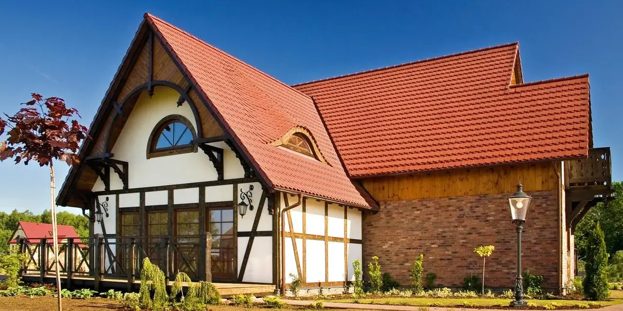 Elegancki dom z charakterystycznym dachem pokrytym czerwoną dachówką karpiówką, otoczony zadbanym ogrodem.