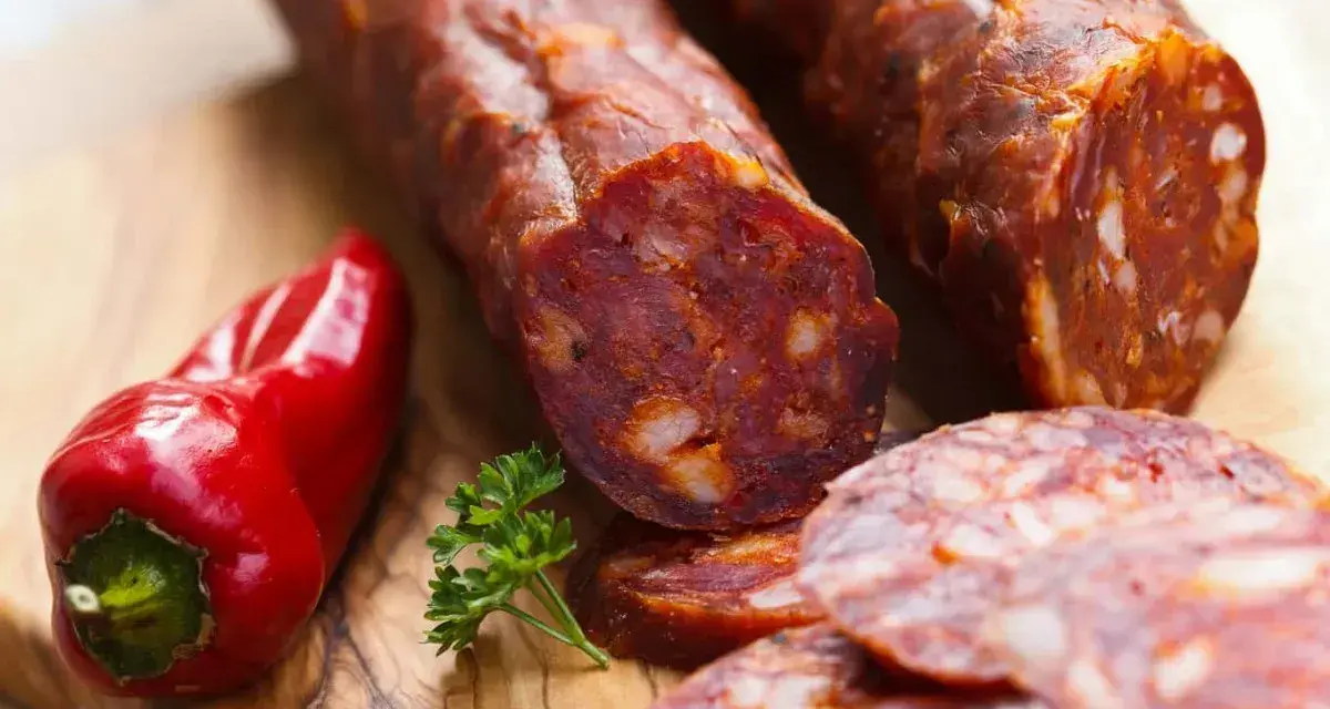 Kawałki pikantnego chorizo, czerwona papryczka i natka pietruszki na desce. Chorizo co to? To aromatyczna kiełbasa!