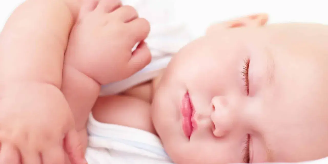 Ein friedlich schlafendes Baby, etwa 4 Monate alt, mit geschlossenen Augen und leicht geöffneten Lippen. Die zarte Haut und die kleinen Händchen sind gut zu erkennen.