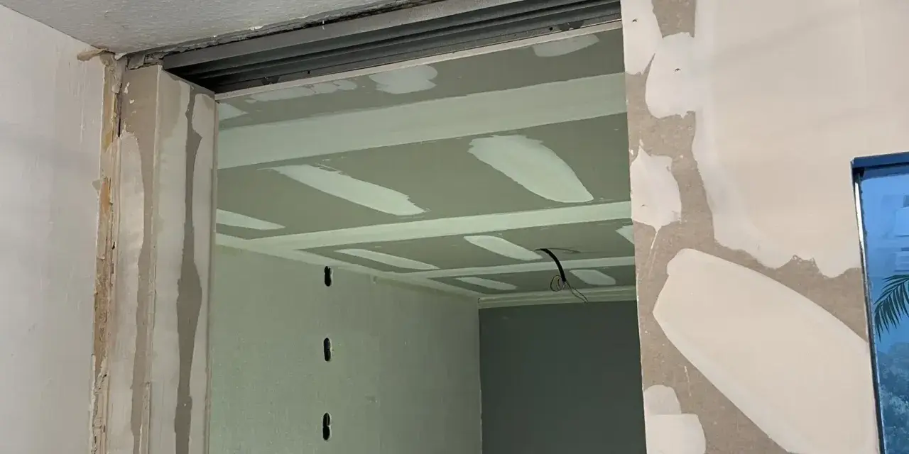 Ouverture dans un mur en cours de travaux de rénovation, avec plaques de plâtre et rails apparents.