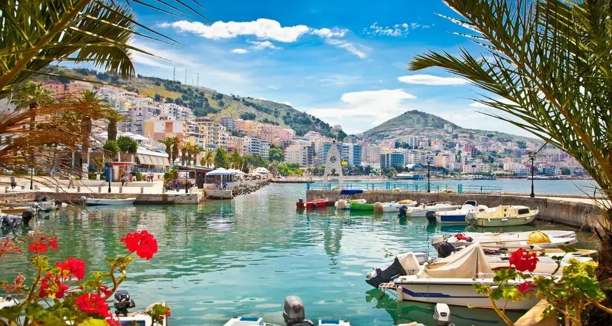 Piękne albania widoki: port z łodziami, palmy i kolorowe miasto na wzgórzu pod błękitnym niebem.