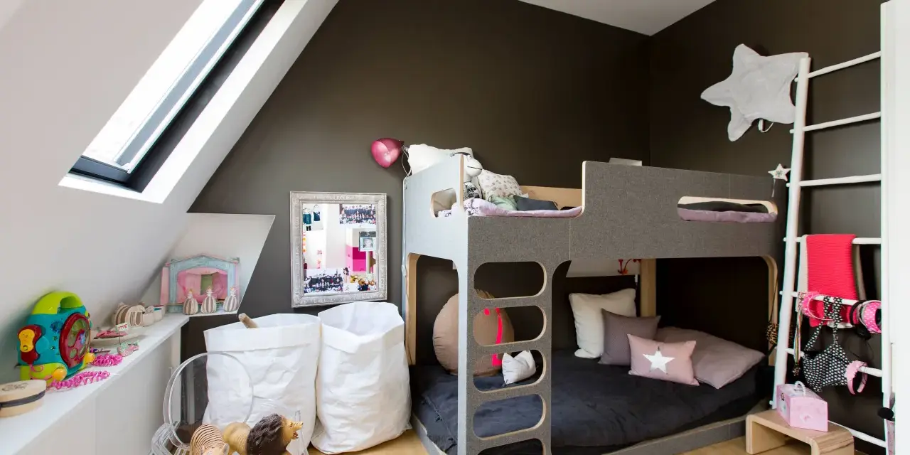 Accogliente camera da letto e cameretta insieme, con letto a castello grigio, giocattoli, cuscini a forma di stella e sacchi bianchi.