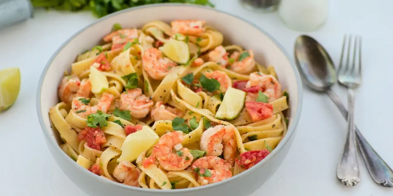 Pyszne tagliatelle z krewetkami, pomidorami i limonką, posypane świeżą natką pietruszki. Idealne danie na szybki obiad.