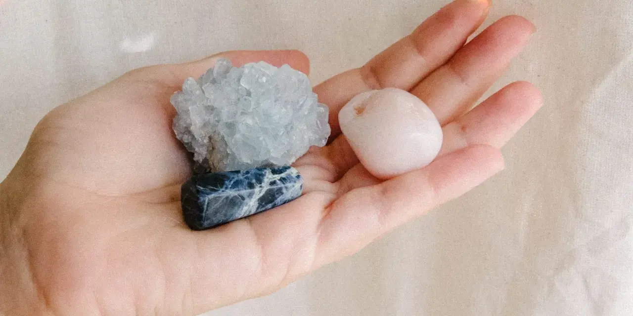 Mano sosteniendo tres piedras: una azul con vetas blancas, una azul pálido cristalina y una rosa pálido pulida. Son piedras para embarazadas.