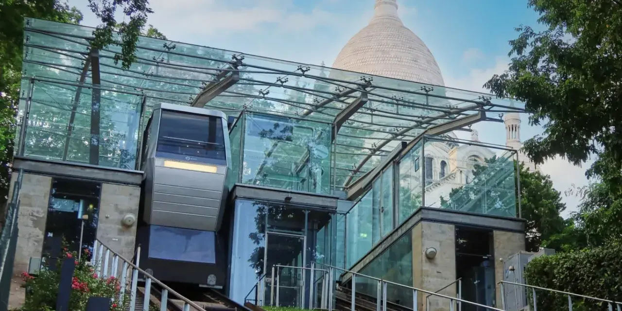 El funicular de Montmartre, con su moderna estación de cristal, asciende hacia la basílica del Sacré-Cœur bajo un cielo azul.