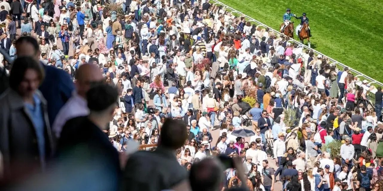 Foule nombreuse sur un hippodrome en France, spectateurs massés pour une course de chevaux.