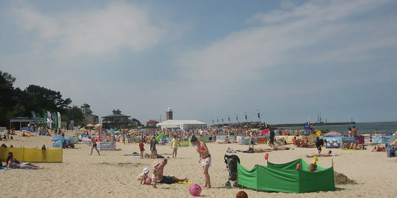Słoneczna plaża w Darłowie tętni życiem. Ludzie opalają się, bawią z dziećmi i odpoczywają pod kolorowymi parawanami.