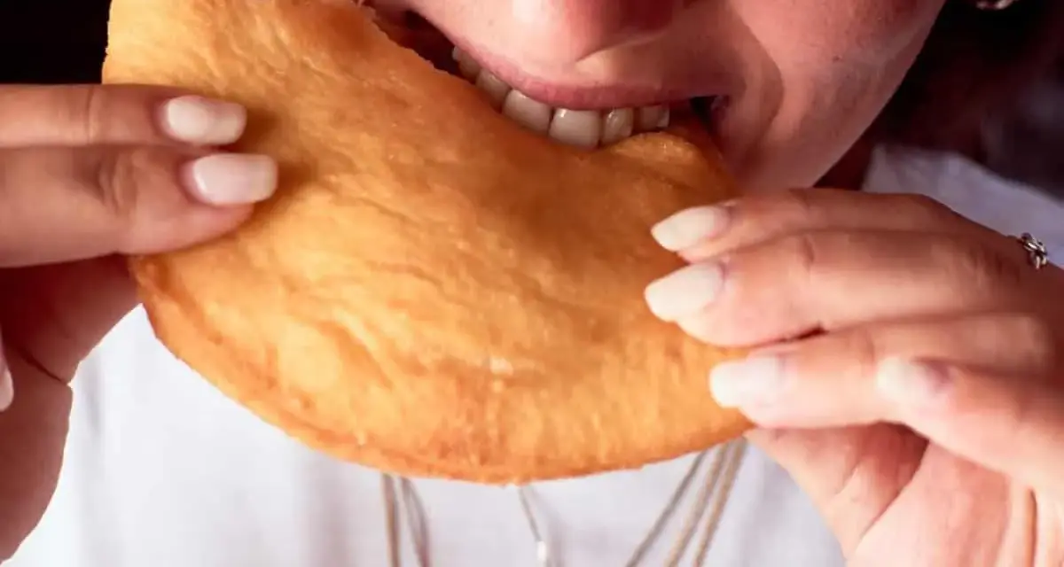 Close-up of a person biting into a golden-brown, fried pastry.