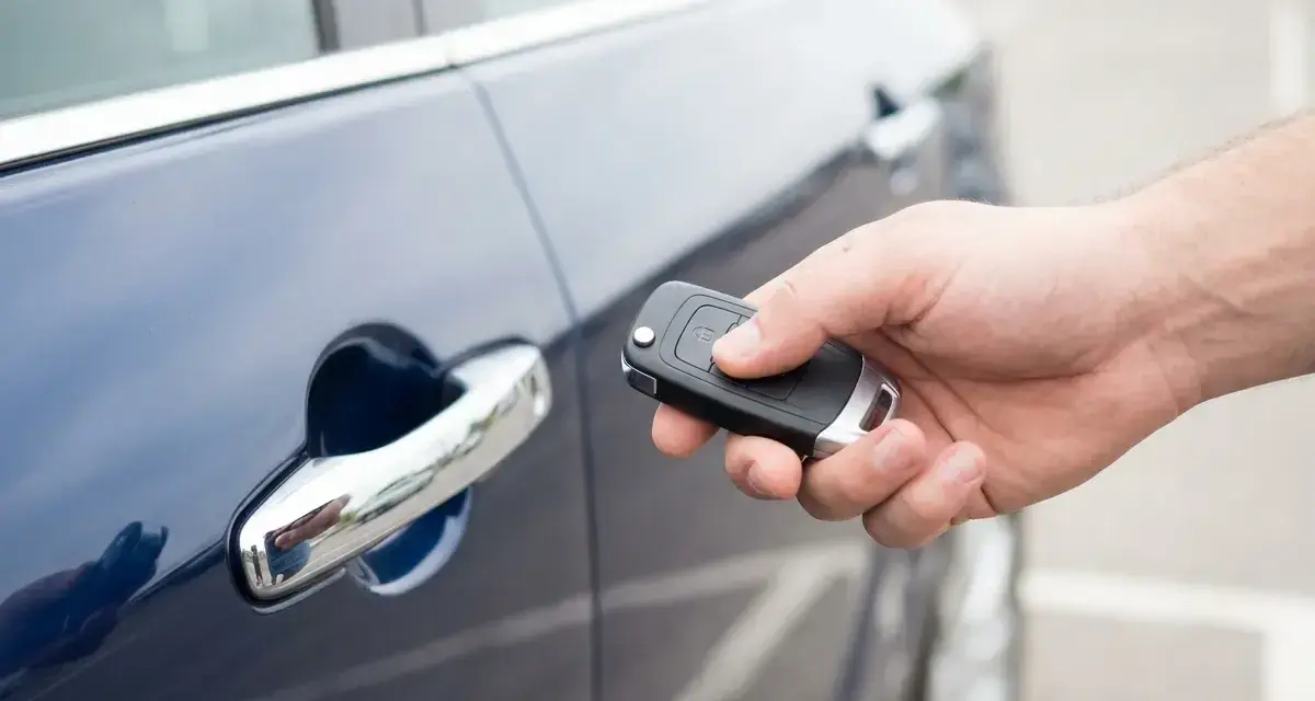 Dłoń trzyma kluczyk keyless, zbliżając go do klamki ciemnoniebieskiego samochodu.
