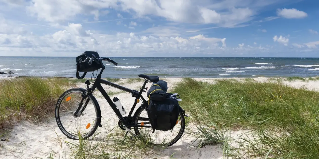 Rower z sakwami na plaży, gotowy do podróży trasą rowerową R10. Morze i niebo w tle.