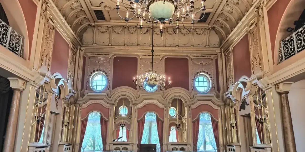 Wnętrze pałacu w Poznaniu, idealne do zwiedzania. Bogato zdobiony sufit, kryształowe żyrandole i eleganckie zasłony tworzą atmosferę dawnej świetności.