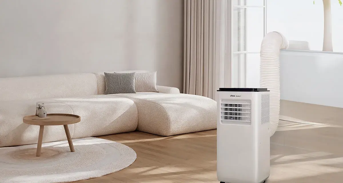 Un aire acondicionado portátil con tubo de escape conectado a la ventana, parte de unas modernas instalaciones hvac, en un salón con sofá beige.