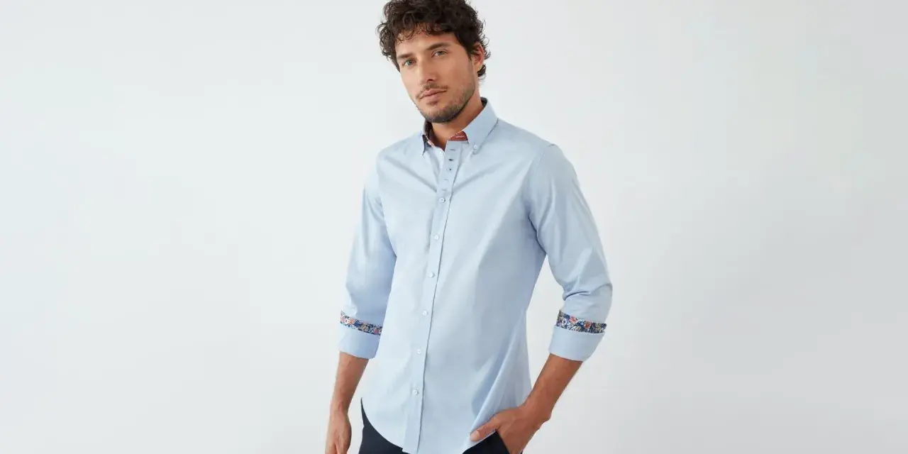 Uomo con camicia blu chiaro, dettagli floreali sui polsini e colletto. Un abbinamento elegante e moderno.
