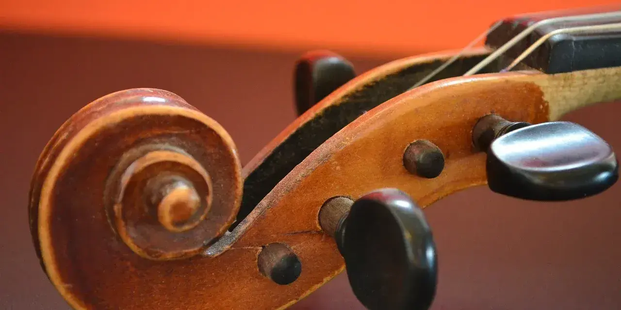 Drewniana ślimacznica skrzypiec, przypominająca spiralę, symbolizuje pierwsze instrumenty muzyczne i ich prostotę.