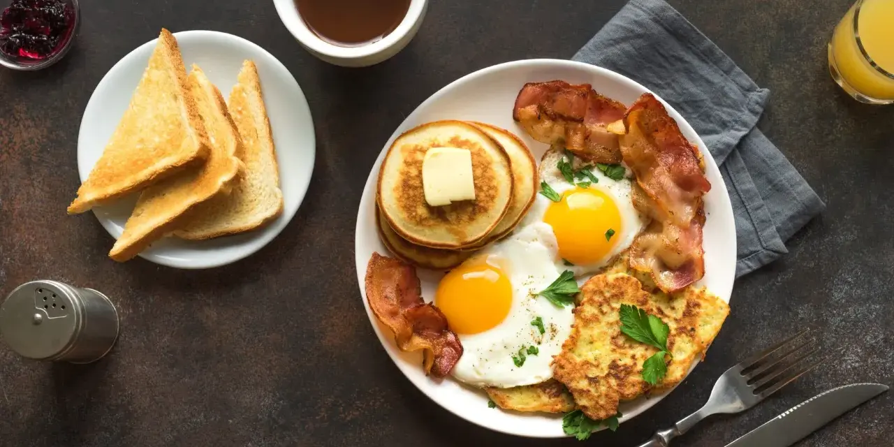 Esempio di colazione proteica per dimagrire: uova, bacon, pancake, toast e succo d'arancia.