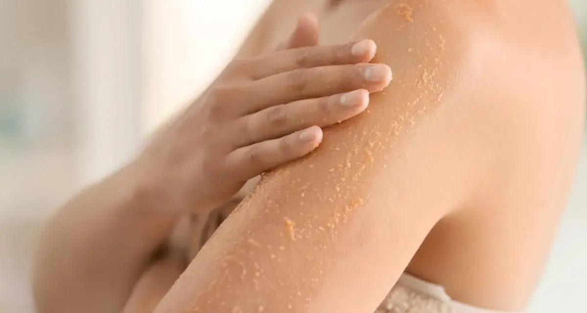 Mano che applica scrub su braccio, rimuovendo la pelle morta dopo la doccia per una pelle liscia e luminosa.