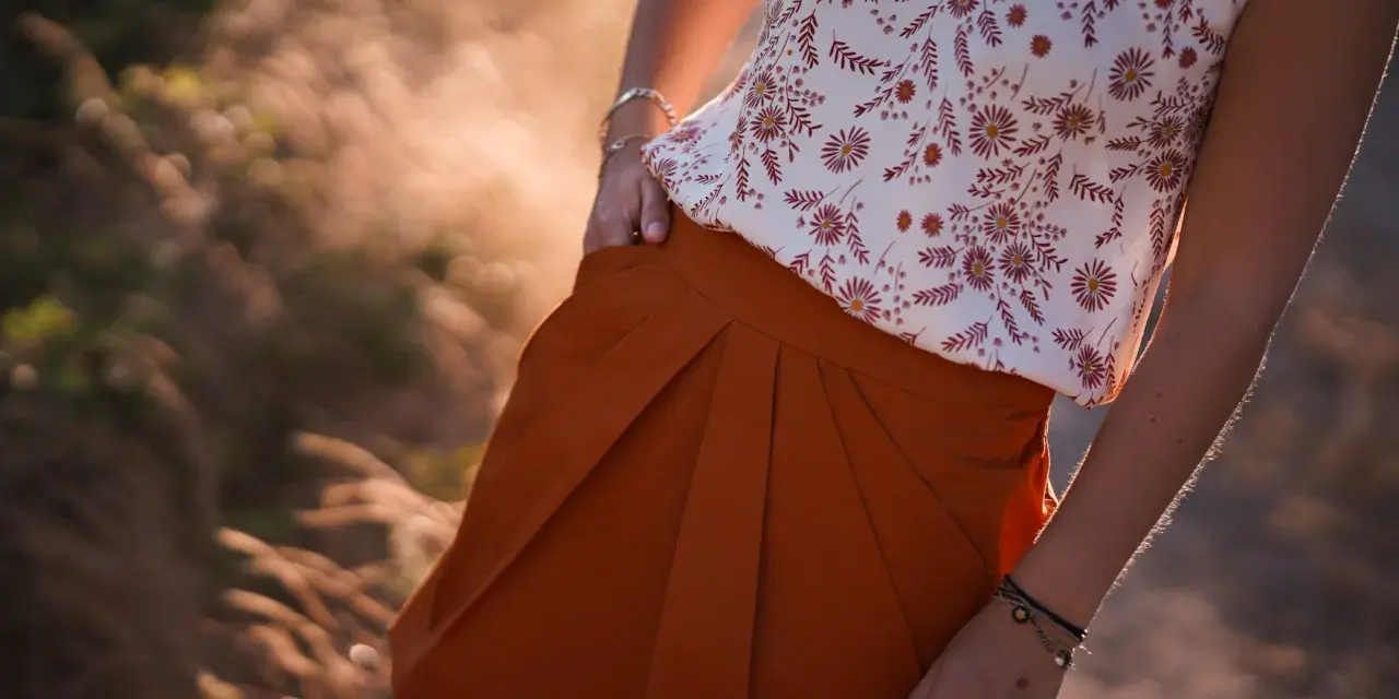 Jupe tulipe orange à plis, portée avec un haut fleuri. Le soleil couchant illumine la scène.