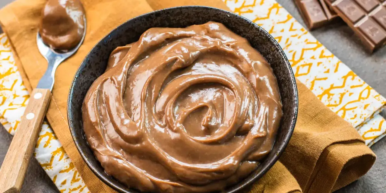 Una ciotola piena di deliziosa crema pasticcera al cioccolato, con una cucchiaiata pronta da gustare. Accanto, una tavoletta di cioccolato.
