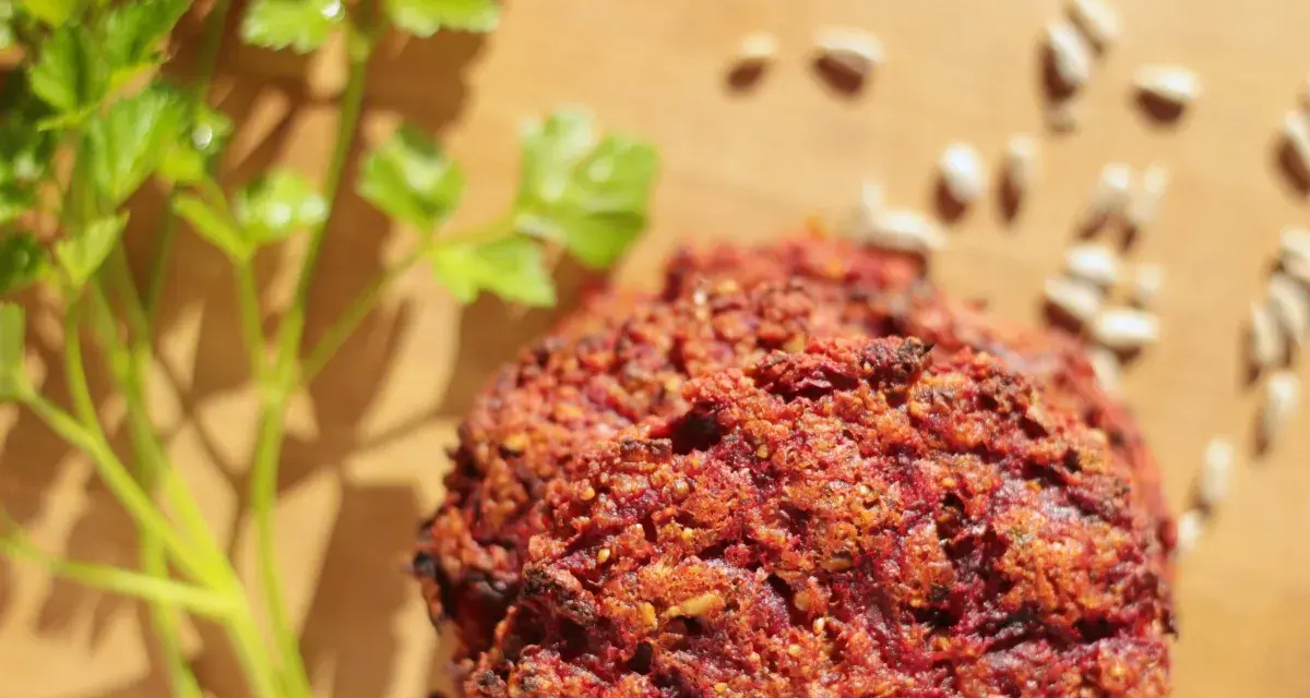 Pyszne kotlety z buraka, przypominające falafel, leżą na desce obok gałązki pietruszki i nasion słonecznika.